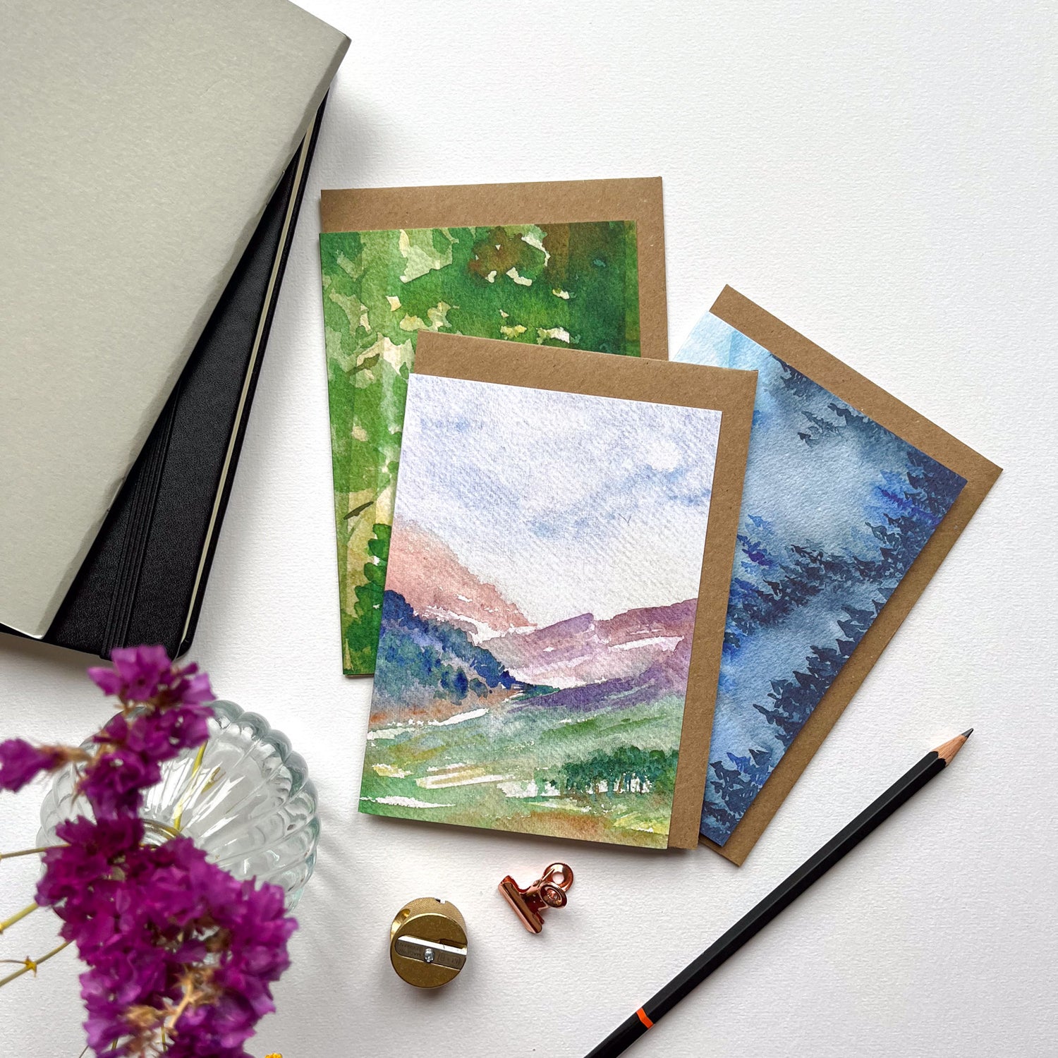 Three greeting cards flat on a table with watercolour landscape designs